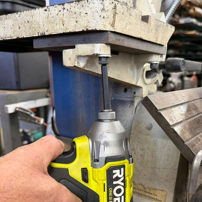 Person using a Ryobi power drill on a metal surface with a workshop background