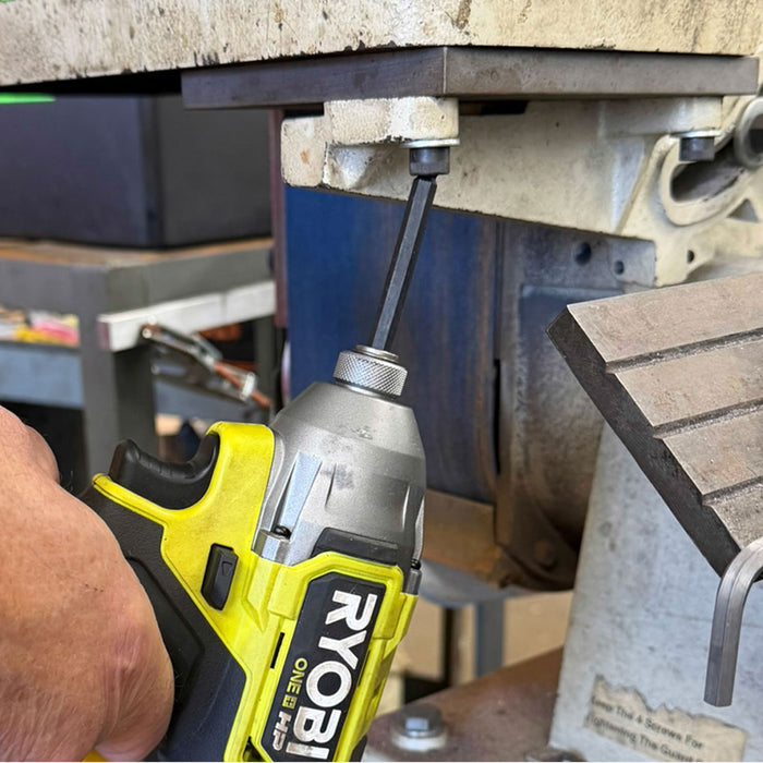 Person using a Ryobi drill on a concrete surface with tools and equipment in the background.