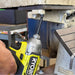 Person using a Ryobi drill on a concrete surface with tools and equipment in the background.