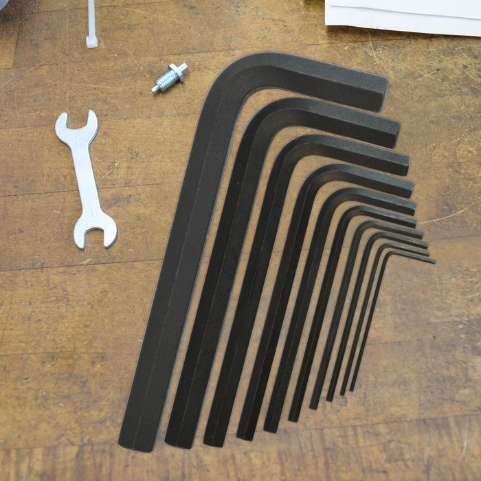 Set of black Allen keys arranged by size on a wooden surface with a white wrench.