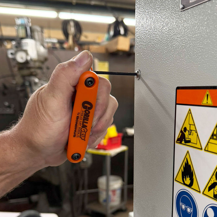 Hand using an orange Gorilla Tool to screw into a metal panel with warning signs.