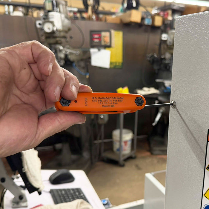 Hand holding an orange tool in a workshop setting