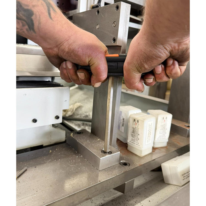 Close-up of hands using a tool on a metal surface with containers in the background