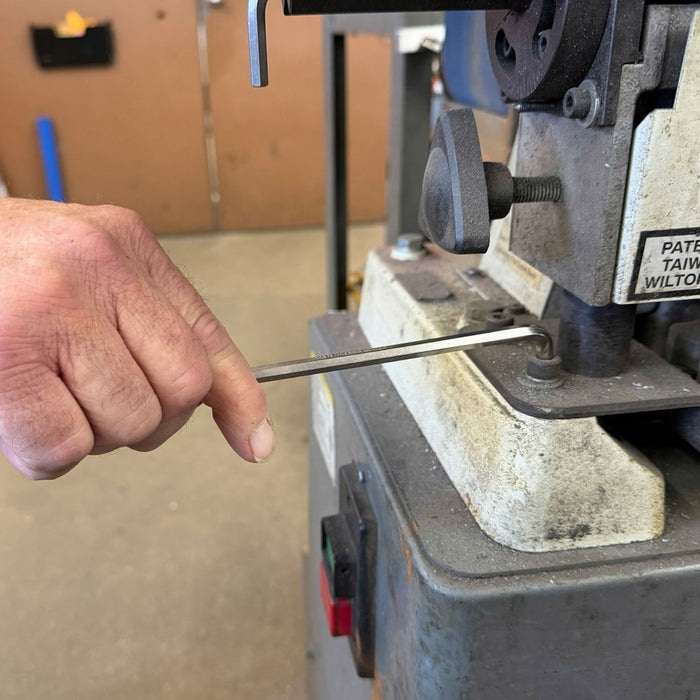 Hand using a metal file on a bench vice in a workshop setting