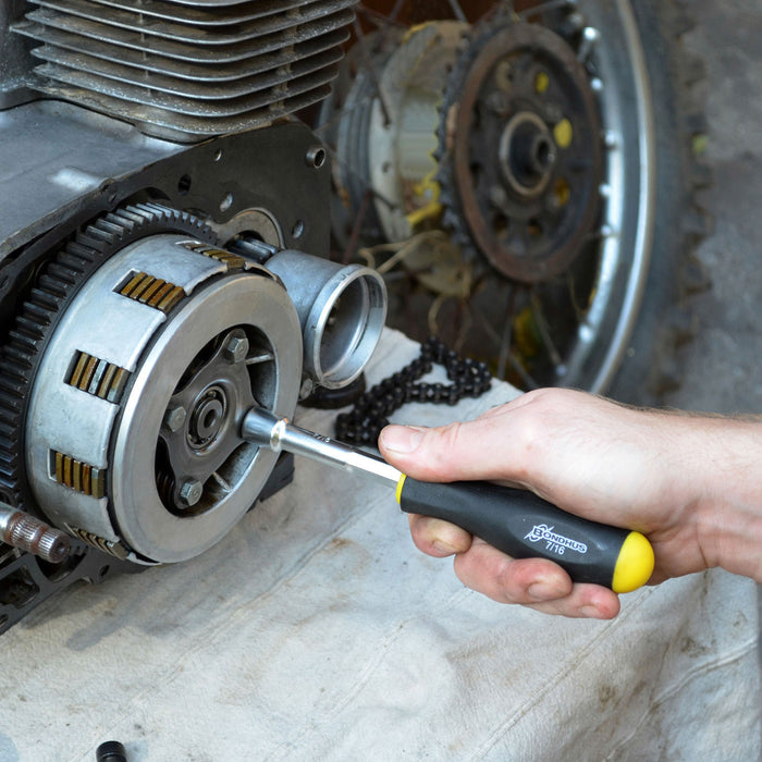 Hand using a screwdriver on a mechanical component with gears in the background