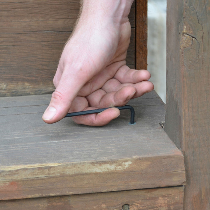 Hand using a black torx L wrench on a wooden surface