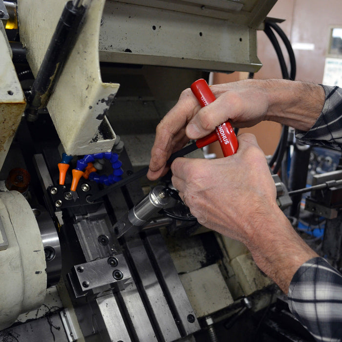 Person using a red tool on a machine in a workshop setting