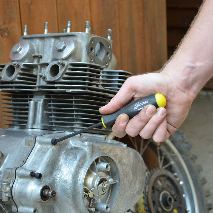 Hand holding a screwdriver near a motorcycle engine