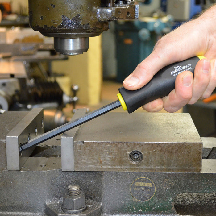 Hand holding a screwdriver near a metal workpiece with machinery in the background