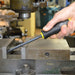 Hand holding a screwdriver near a metal workpiece with machinery in the background