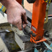 Person using a tool to adjust an orange metal component on a machine.