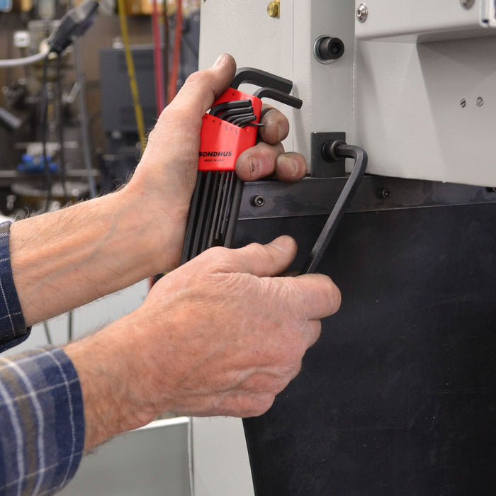 Person using a tool set with a red handle on a mechanical device in a workshop setting.