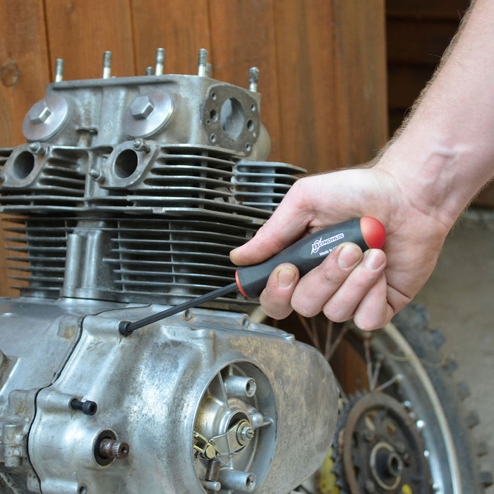 Hand holding a screwdriver near a motorcycle engine