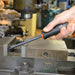 Hand using a screwdriver on a metal surface with machinery in the background