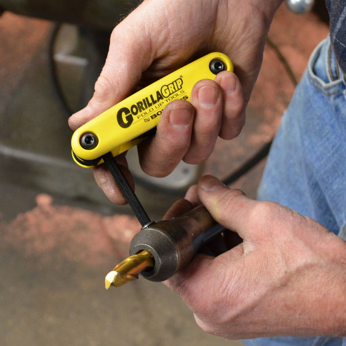 Hand holding a yellow GorillaGrip tool with a drill bit attached, blurred background