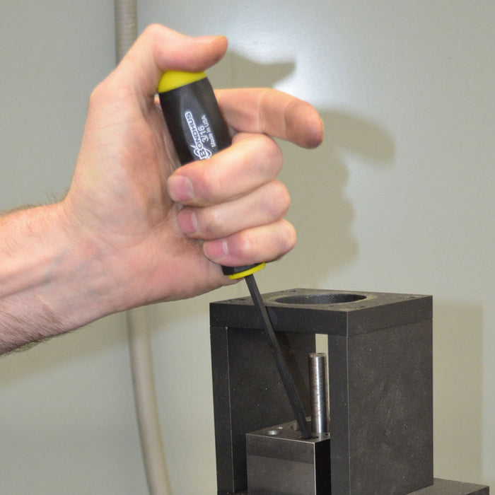 Hand using a screwdriver with yellow end to work on a metal component against a neutral background